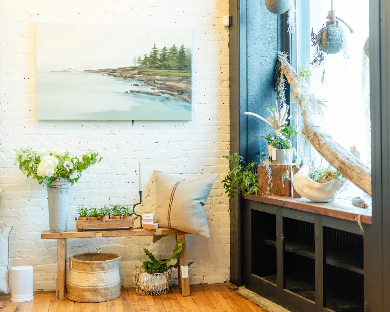 A styled corner at STELLAN in Portland: white brick, a coastal painting, and a bench of textiles by the window