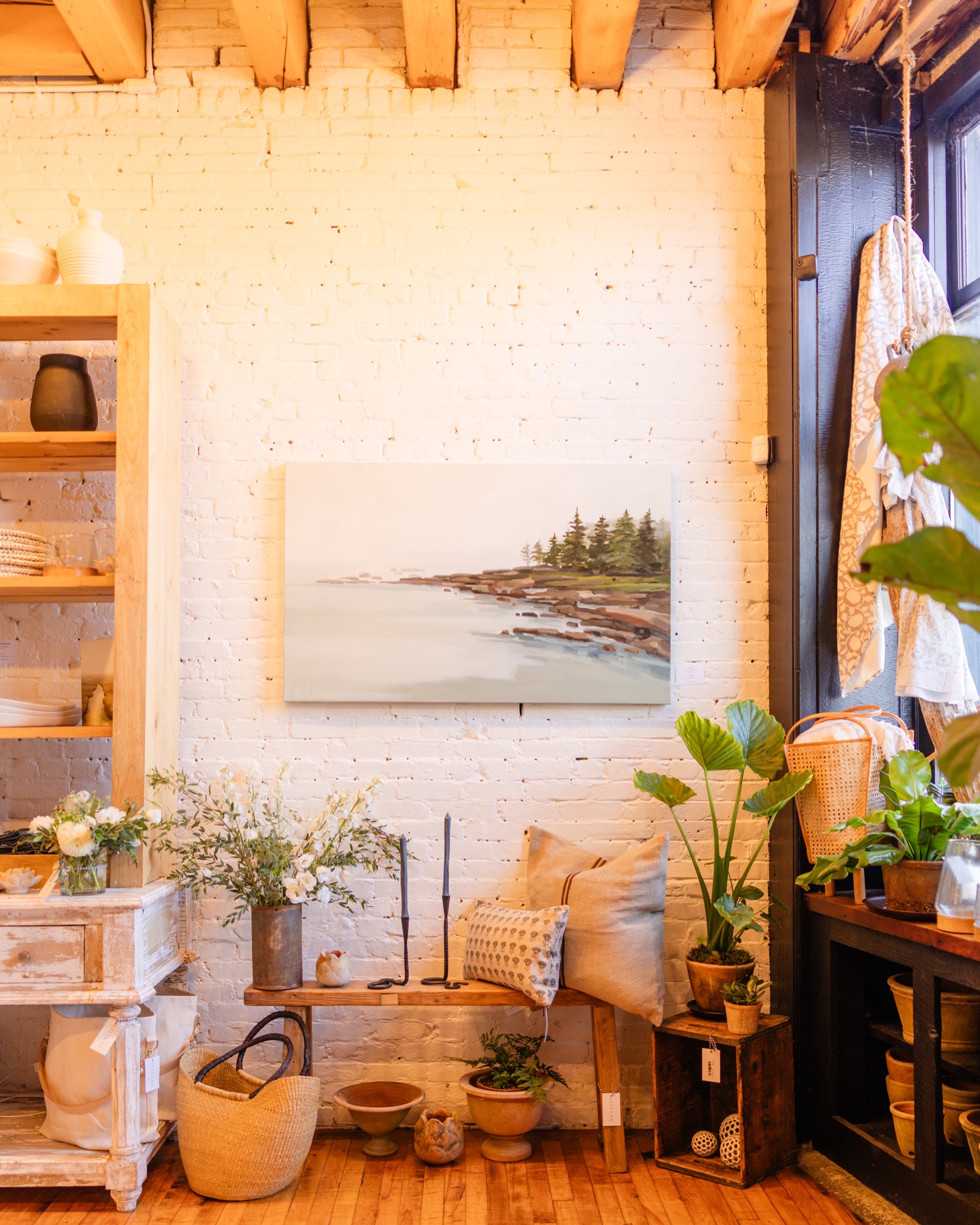 A coastal painting over a bench of pillows and plants